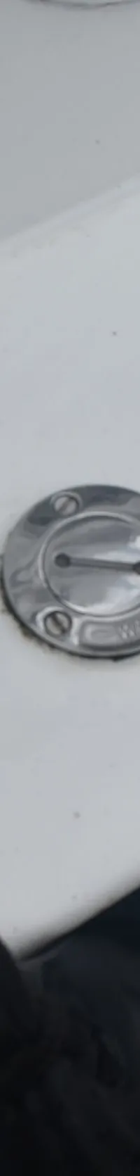 Een witte boot met een zwarte lijn, een zilveren kikker en een zilveren waterdop, naast donker water en een houten steiger.