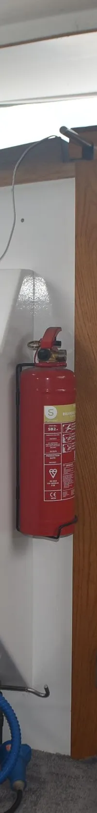 De foto toont een stuurstand met een wit stuur, een witte stoel, een rood brandblusapparaat en houten deuren.