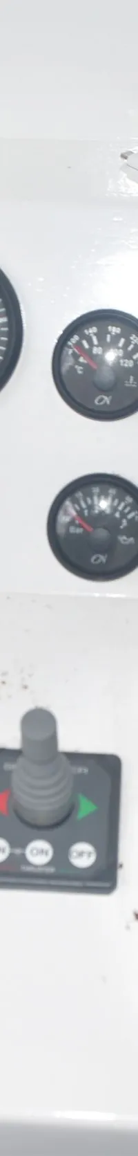 Een wit bedieningspaneel met diverse meters, schakelaars, een joystick en een gashendel, naast een rode brandblusser en een…