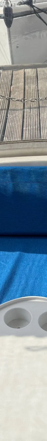 De foto toont een bootinterieur met blauwe kussens en een witte tafel, met uitzicht op een steiger en andere boten.