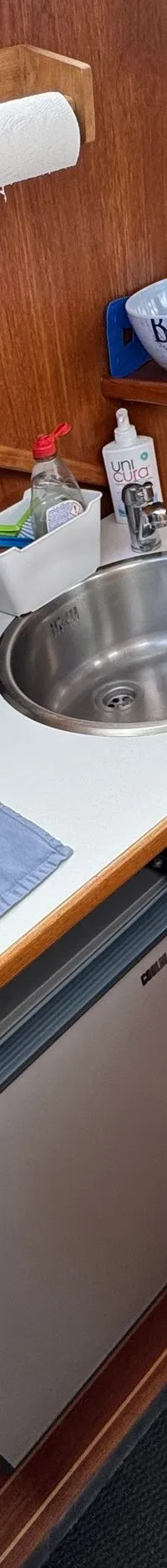 Een kombuis met een spoelbak, waterkoker, afwasbak, koelkast en een theedoek op een houten vloer.