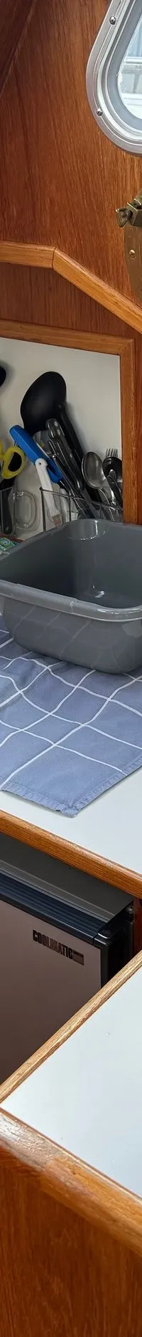 Een kombuis met een aanrecht, spoelbak, koelkast, waterkoker, thermoskan en diverse keukenbenodigdheden.