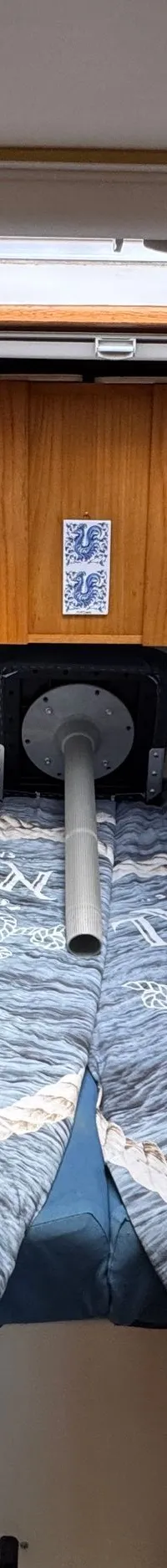 De foto toont de kajuit van een boot met een V-vormig bed, patrijspoorten, een dakluik en houten kasten.