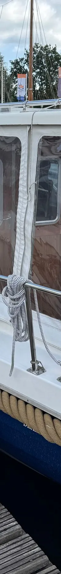 Een witte boot met blauwe romp en een bruine stootrand ligt afgemeerd aan een houten steiger. — Drammer 8.20 Classic