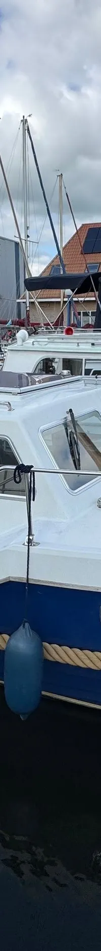 Een witte en blauwe motorboot met de naam "Balance" ligt aangemeerd in een haven, omringd door andere boten en gebouwen.