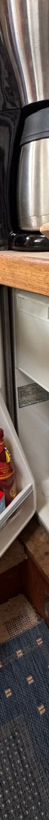 Een open koelkast en vriezer in een houten interieur met een koffiezetapparaat en waterkoker op het aanrecht.