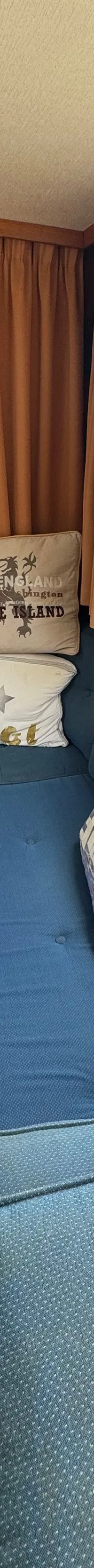 De foto toont het interieur van een boot met blauwe banken, een houten tafel en een uitzicht op andere boten in een haven.