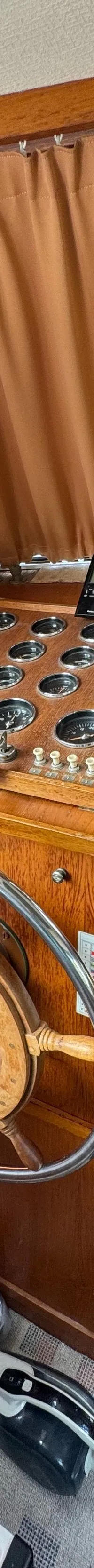 De foto toont het interieur van een boot met een houten stuurwiel, een dashboard vol meters en bedieningshendels.