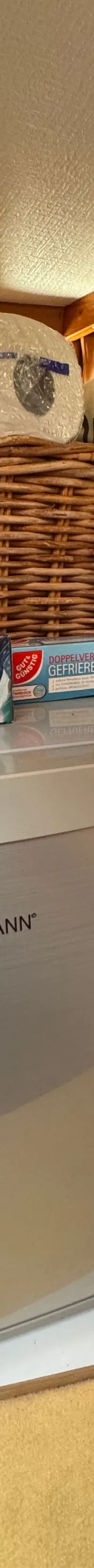 Een zilverkleurige Bomann koelkast staat op een houten plank, met een fles sap ernaast en een rieten mand erboven.