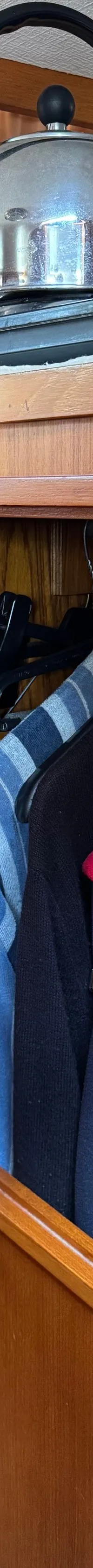 Een open kast met kleding hangend aan hangers en een waterkoker op een kookplaat erboven.