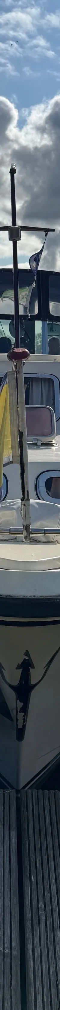 Een witte motorboot ligt aangemeerd aan een houten steiger, met een gele vlag aan de boeg en stootwillen aan de zijkanten.