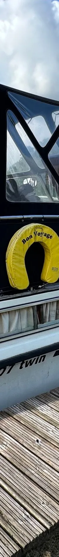 Een witte motorboot met zwarte kap en gele reddingsboei ligt aangemeerd aan een houten steiger. — Neptunus 107 TWIN