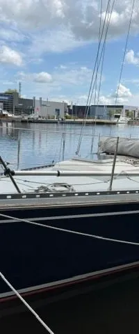 Een blauw-witte zeilboot ligt afgemeerd aan een kade, met een gebouw en andere boten op de achtergrond. — Victoire 34 S-spant