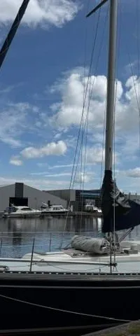 Een donkerblauwe zeilboot met een witte opbouw ligt aangemeerd aan een kade, met een blauwe zeilhoes met de naam "JODZERT".
