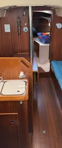 De foto toont het interieur van een boot met een kombuis, zithoeken met blauwe kussens en een navigatiehoek.