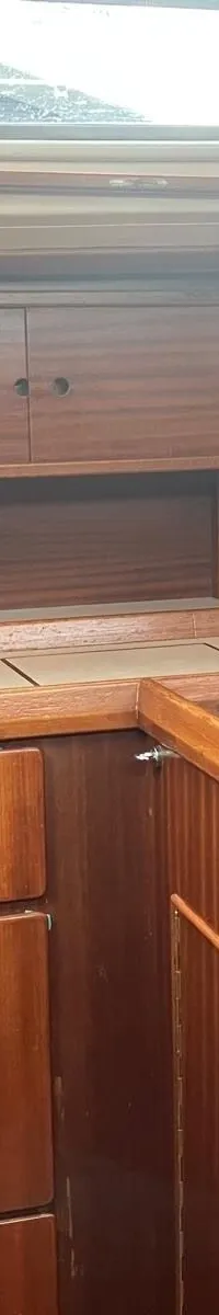 De foto toont een houten interieur van een boot met een kombuis, inclusief een fornuis, gootsteen en opbergruimte.