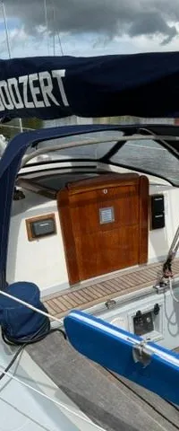 Een zeilboot met een blauwe buiskap en een zeilhoes met de tekst "JOOZEPT" ligt aangemeerd aan een kade.