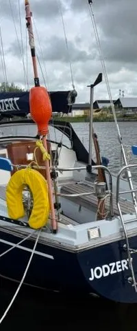 Een donkerblauwe zeilboot met de naam "JODZER" en "LEEUWARDEN" op de spiegel, ligt afgemeerd aan een kade.