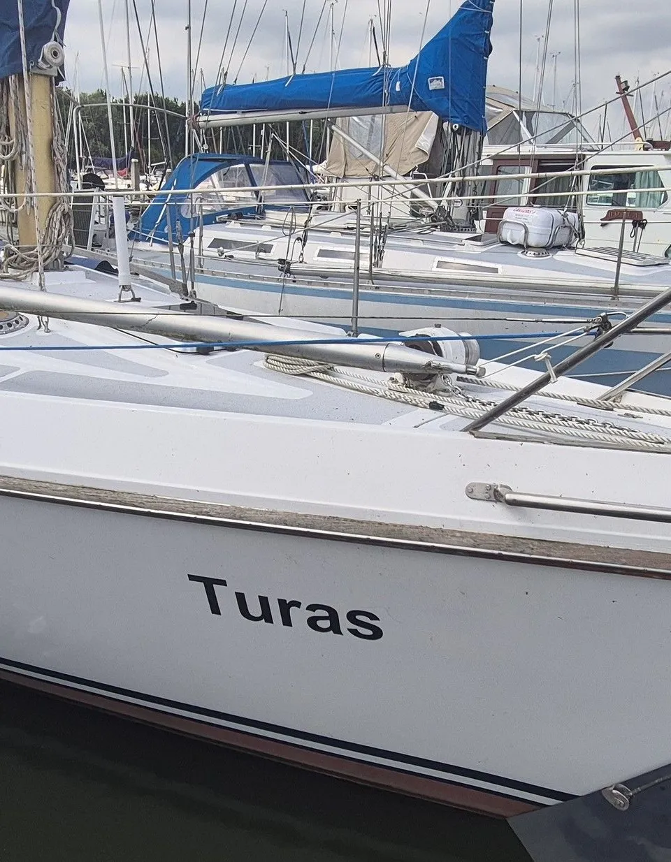 Een witte zeilboot genaamd "Turas" ligt afgemeerd in een haven met andere boten op de achtergrond. — Contest 36 Ketch