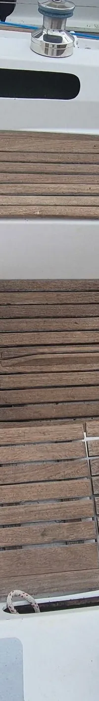 Een bovenaanzicht van de kuip van een zeilboot met een houten vloer, stuurwiel, navigatie-instrumenten en een blauw zeil.