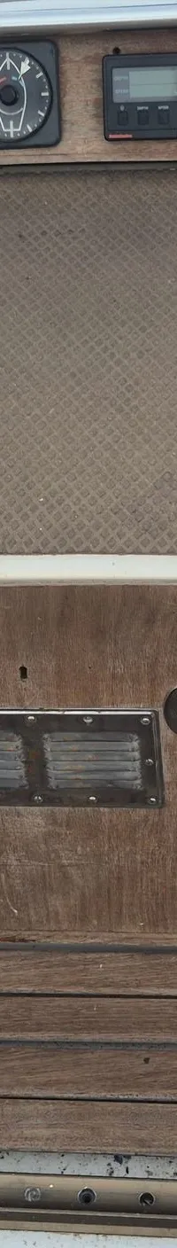 Een bovenaanzicht van een bootdek met houten panelen, instrumenten en een Raymarine marifoon.