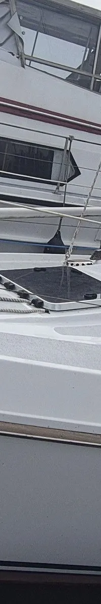 Een witte zeilboot met de naam "Turas" ligt afgemeerd naast een steiger, met een andere boot op de achtergrond.