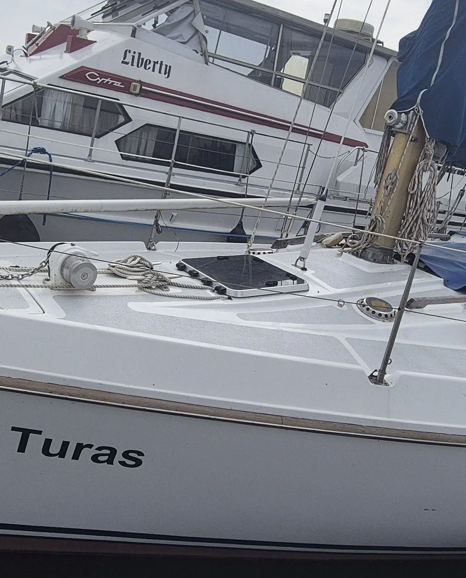 Een witte zeilboot met de naam "Turas" ligt afgemeerd naast een steiger, met een andere boot op de achtergrond.