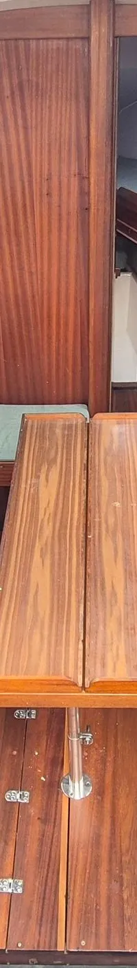 De foto toont het interieur van een boot met houten wanden, een tafel, twee banken met lichtblauwe kussens en een kookplaat.