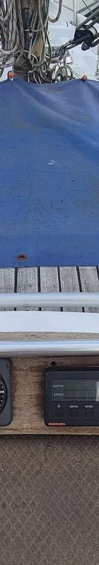 Een bovenaanzicht van het dek van een zeilboot met een blauw zeil, houten details en diverse navigatie-instrumenten.