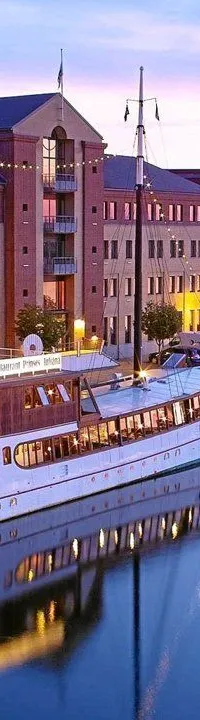 Een grote witte boot met houten opbouw en verlichte ramen ligt aangemeerd in een haven, met de naam "PRINSES JULIANA…