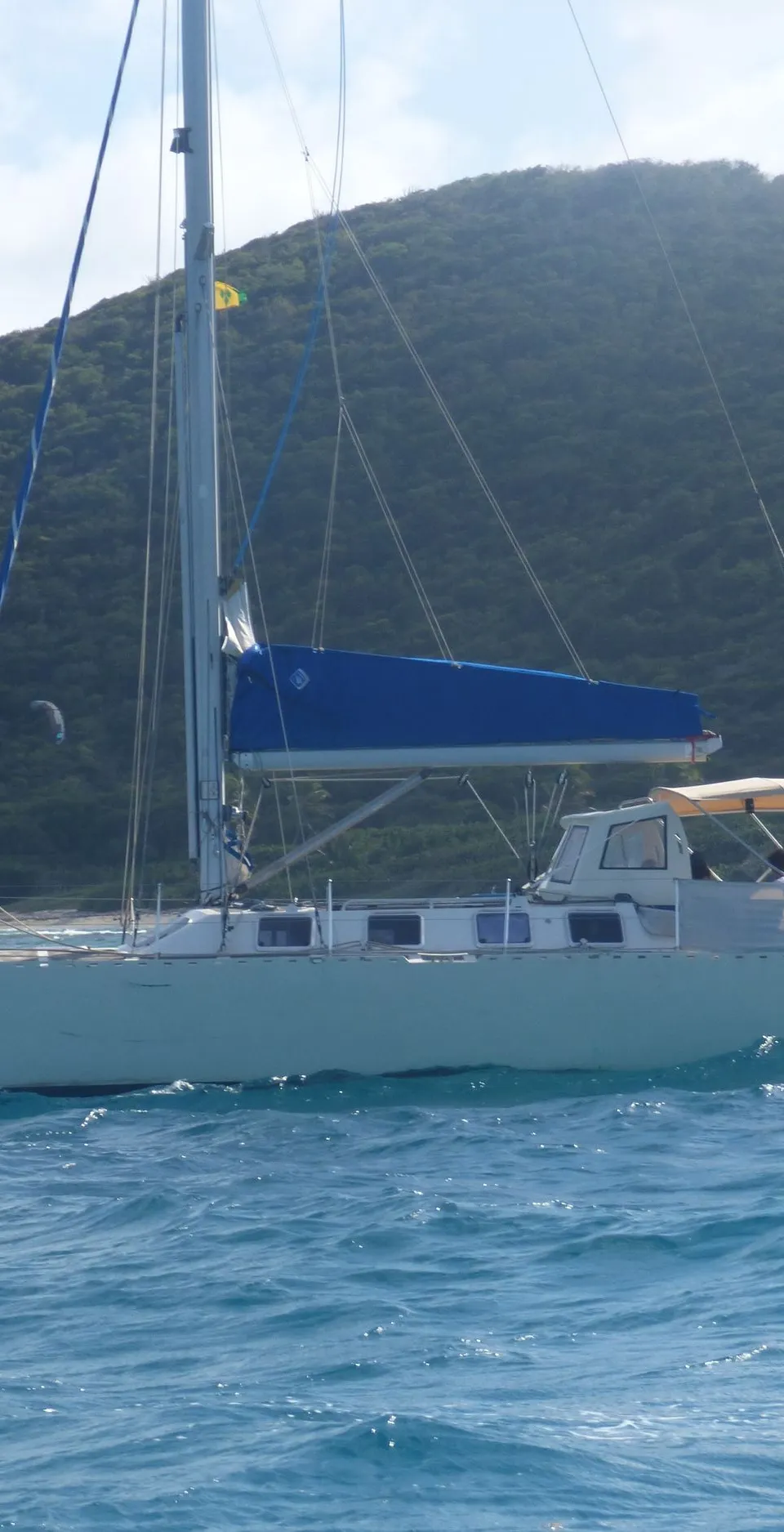 Een zeilboot met de naam "Tepee" op de boeg vaart op blauw water voor een groene, heuvelachtige kustlijn. — Navalu Faré 42