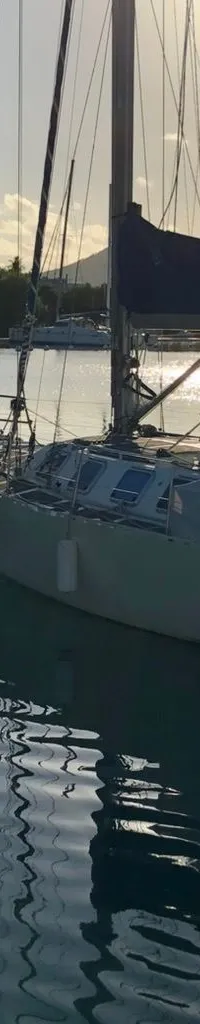 Een zeilboot met een persoon op de boeg ligt in het water, met een deels opgerold grootzeil en fenders aan de zijkant.