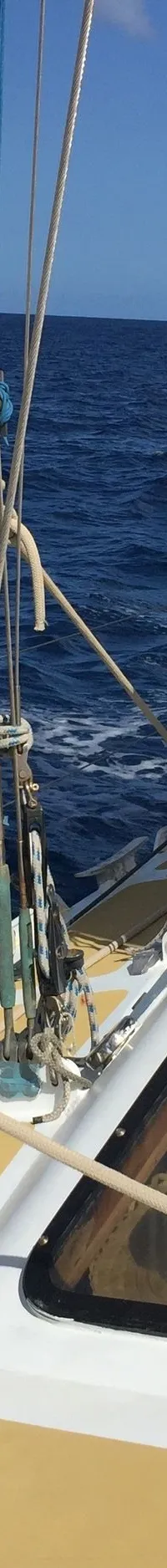 Een zeilboot vaart op open water met een deels uitgerold wit zeil met blauwe band, en een persoon op het dek.