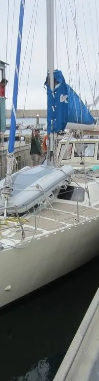 Een lichtgekleurde zeilboot met de naam "Tepee" op de boeg ligt in het water naast een hijskraan in een haven.