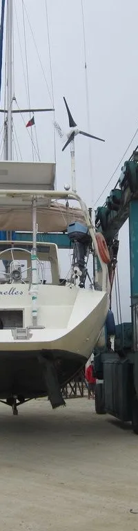 Een zeilboot met de naam "Bruxelles" op de spiegel wordt door een blauwe botenlift op het droge getild, met andere boten op…