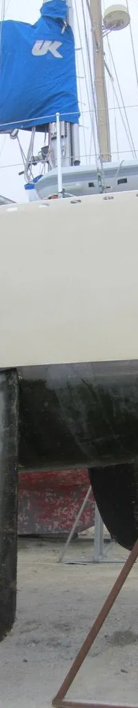 Een zeilboot staat op de wal, ondersteund door stutten, met een blauwe zeilhoes met "UK" en een witte stootwil.