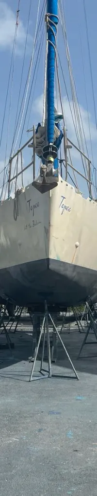 Een zeilboot genaamd 'Tepee' staat op bokken in een botenwerf, met een catamaran en gebouwen op de achtergrond.