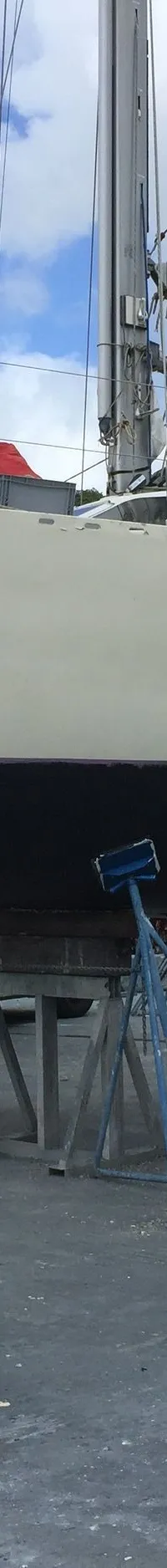 Een lichtgekleurde zeilboot met de naam "Tepee" op de boeg staat op bokken op de wal, met een opgerold blauw zeil.
