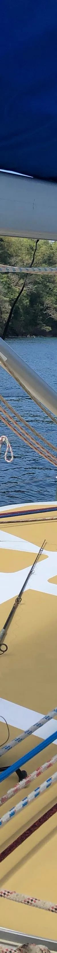 Het dek van een zeilboot met een geel-wit patroon, een blauwe zeilhuik, lijnen en een vishengel is zichtbaar.