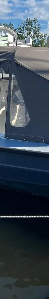 Een donkergrijze motorboot met een lichtgrijs dek en een donkergrijze buiskap ligt afgemeerd aan een steiger.