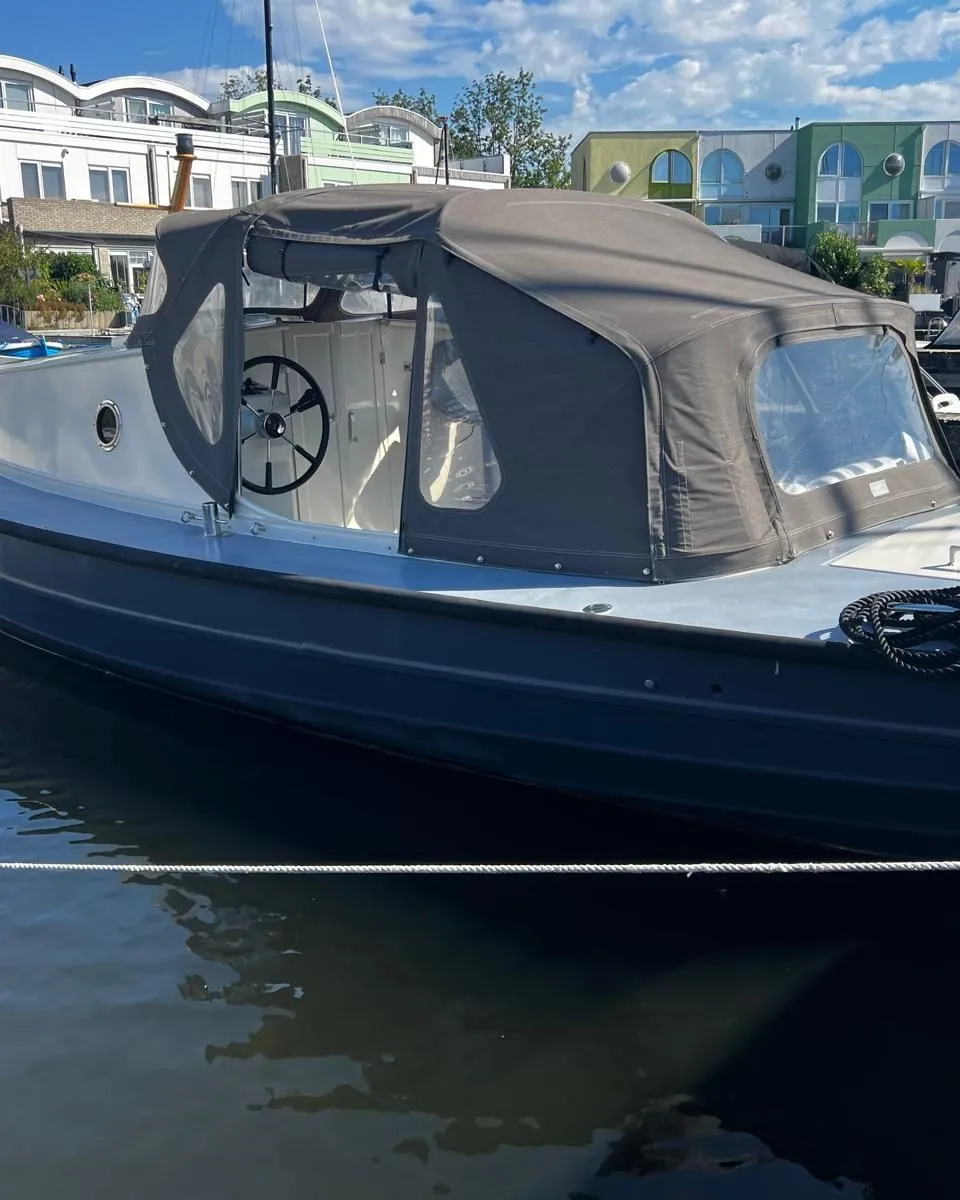 Een donkergrijze motorboot met een lichtgrijs dek en een donkergrijze buiskap ligt afgemeerd aan een steiger.