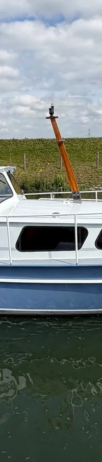 Een blauw-witte motorboot met de naam "LuVa" vaart op een waterweg met een dijk en gebouwen op de achtergrond.