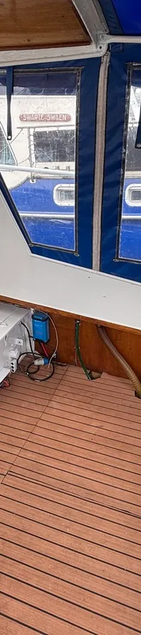 De foto toont het interieur van een boot met houten vloer, witte wanden, houten kasten en blauwe kussens.