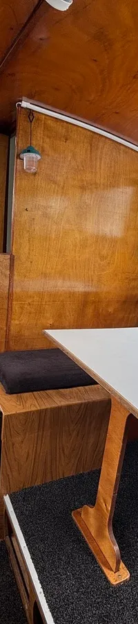 De foto toont het interieur van een boot met houten wanden, een keukenblok, een tafel met banken en een doorgang naar buiten.