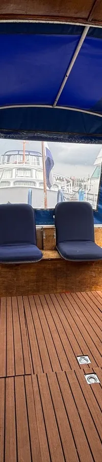 De foto toont het interieur van een boot met een blauwe kap, houten vloer en twee blauwe stoelen. — Ariadne kruiser 900 OK
