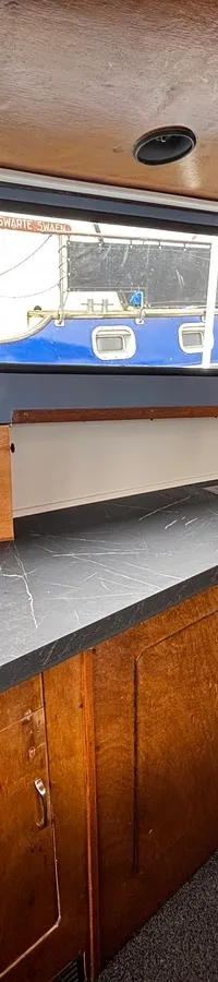 De foto toont een bootinterieur met een aanrechtblad, gootsteen, houten kasten en ramen die uitkijken op een andere boot.