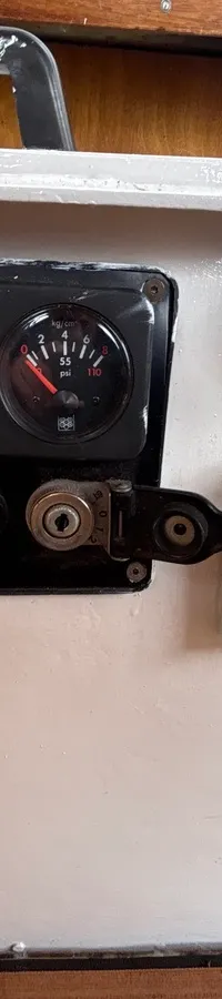 Een wit paneel met twee ronde meters, een spanningsmeter, diverse knoppen en een houten vloer met zwarte naden.