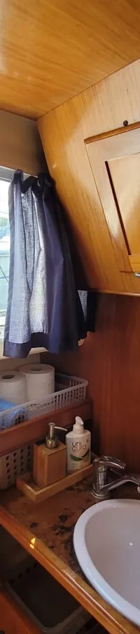 Een houten interieur van een boot met een wastafel, een raam met gordijnen en een opbergvak. — Agder 840 OK