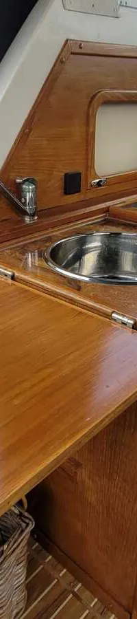 Een houten kombuis met een ronde spoelbak, kraan, een opklapbaar werkblad en een kookplaat met deksel.