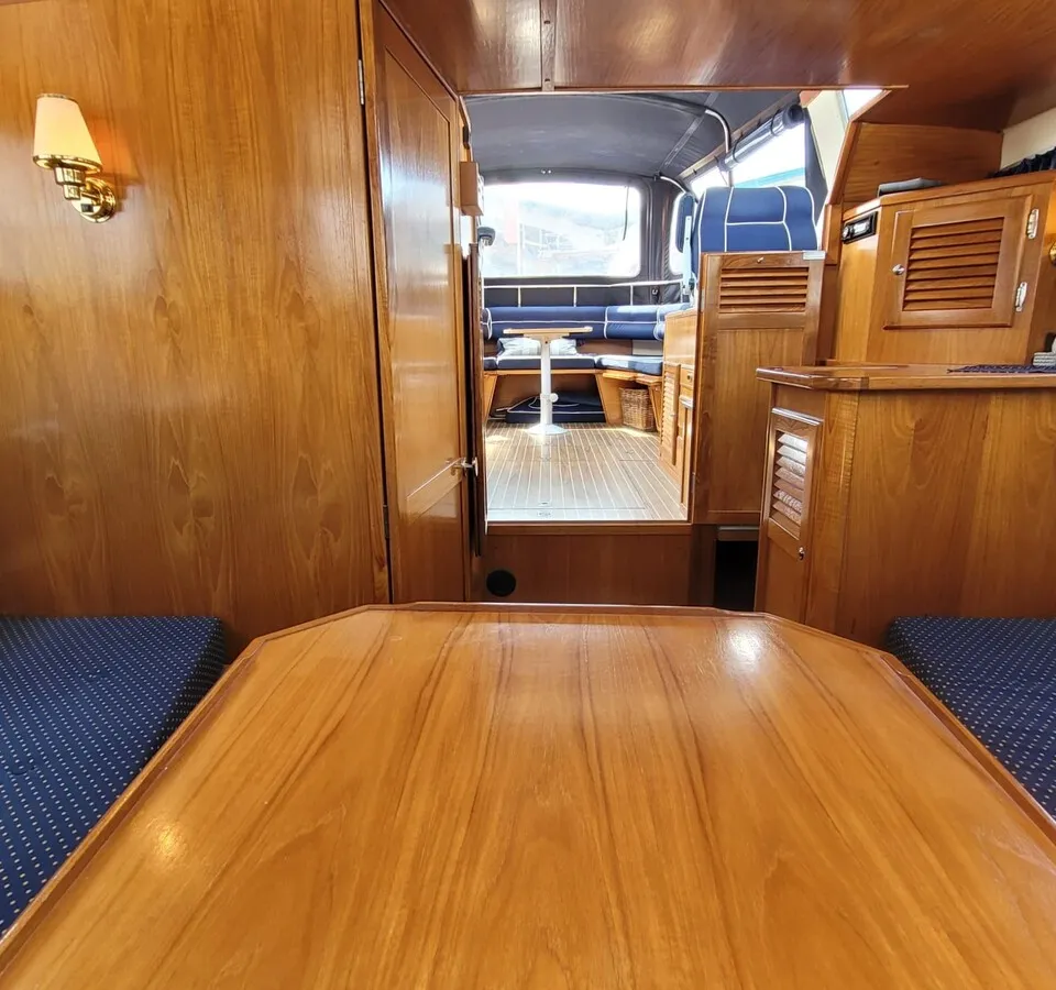 Een interieur van een boot met houten wanden, een houten tafel en blauwe kussens met witte stippen. — Agder 840 OK